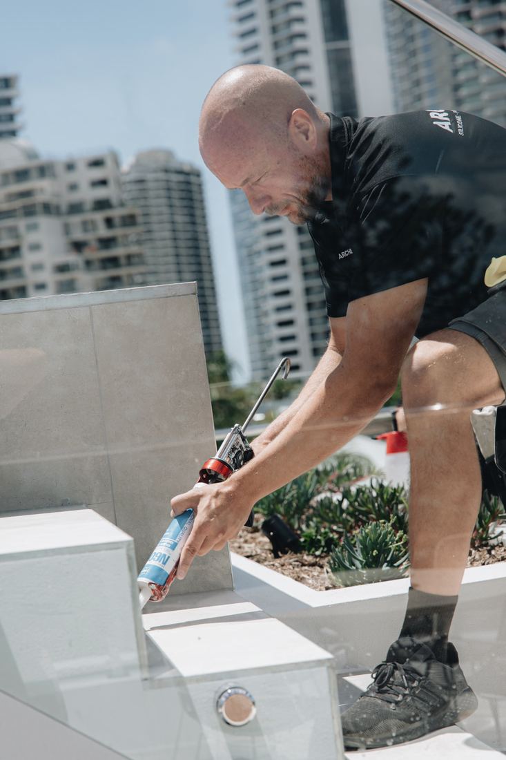 Technician gunning silicone on a rooftop stone parapet